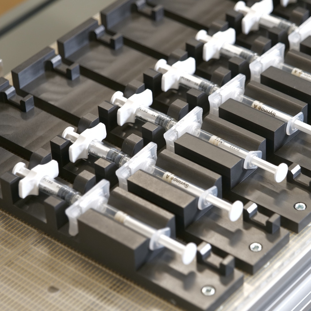 Close-up view of industrial conveyor belt with precision-machined aluminum nests designed for transporting syringe-like medical devices, showcasing advanced medical technology and industrial automation.